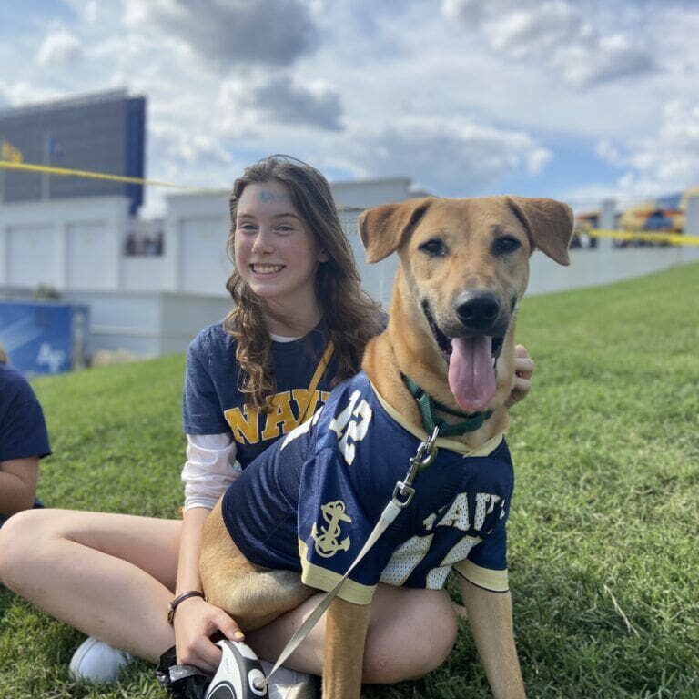 A girl in a navy uniform sitting on the grass with a dog.